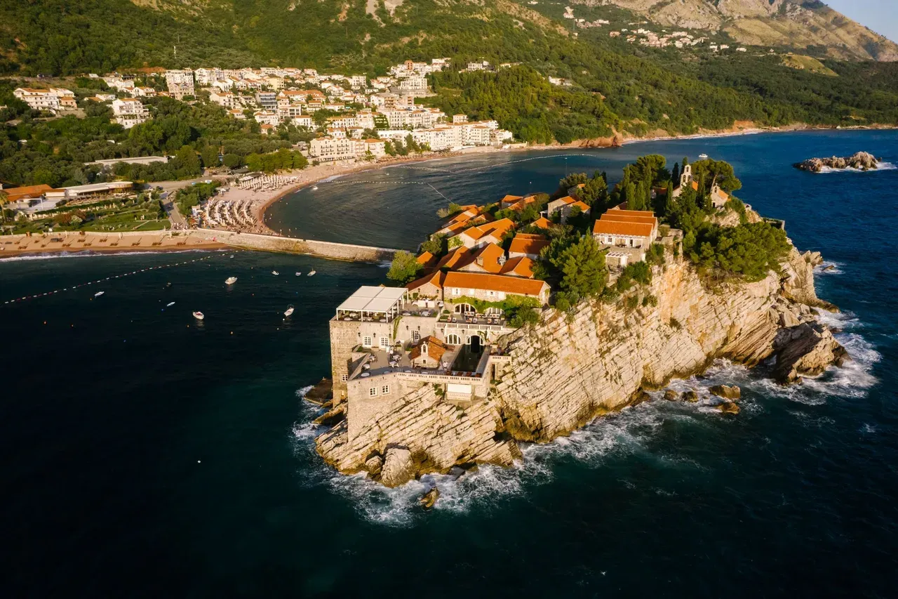 Ostrvo Sveti Stefan iz vazduha — crveni krovovi na stjenovitom ostrvu, plaža i prevlaka